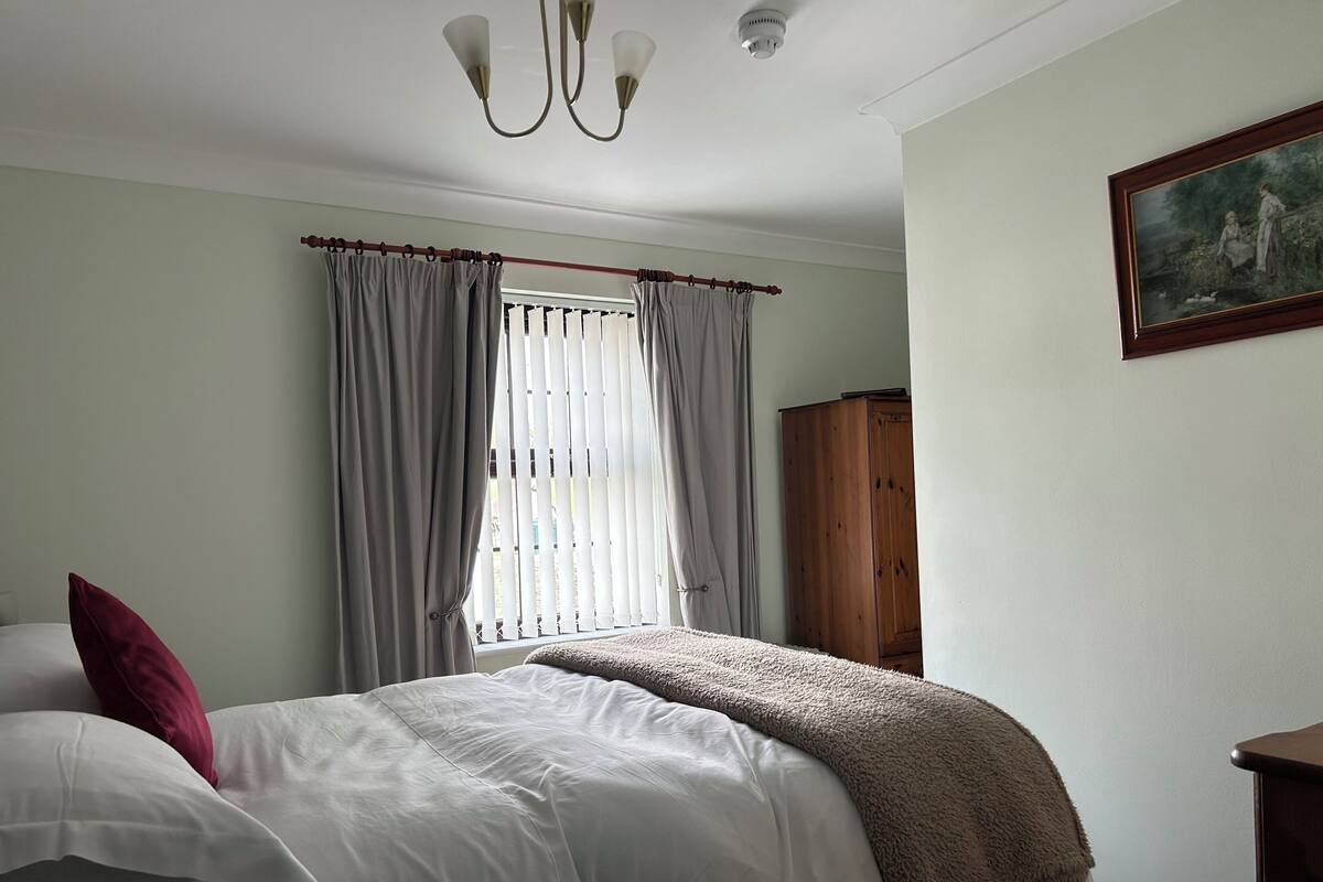 A bedroom with a bed, curtains, a wooden wardrobe, and a painting on the wall.