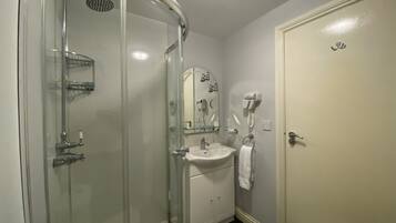 Un baño con cabina de ducha de vidrio, lavamanos con espejo y un perchero para toallas.