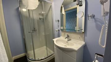 Un baño moderno con cabina de ducha de vidrio, un lavabo blanco y un espejo con secador incorporado.
