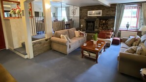 A spacious living room with a fireplace, a staircase leading to another level, and a large window with curtains. - Flambards Hotel (Cardigan)