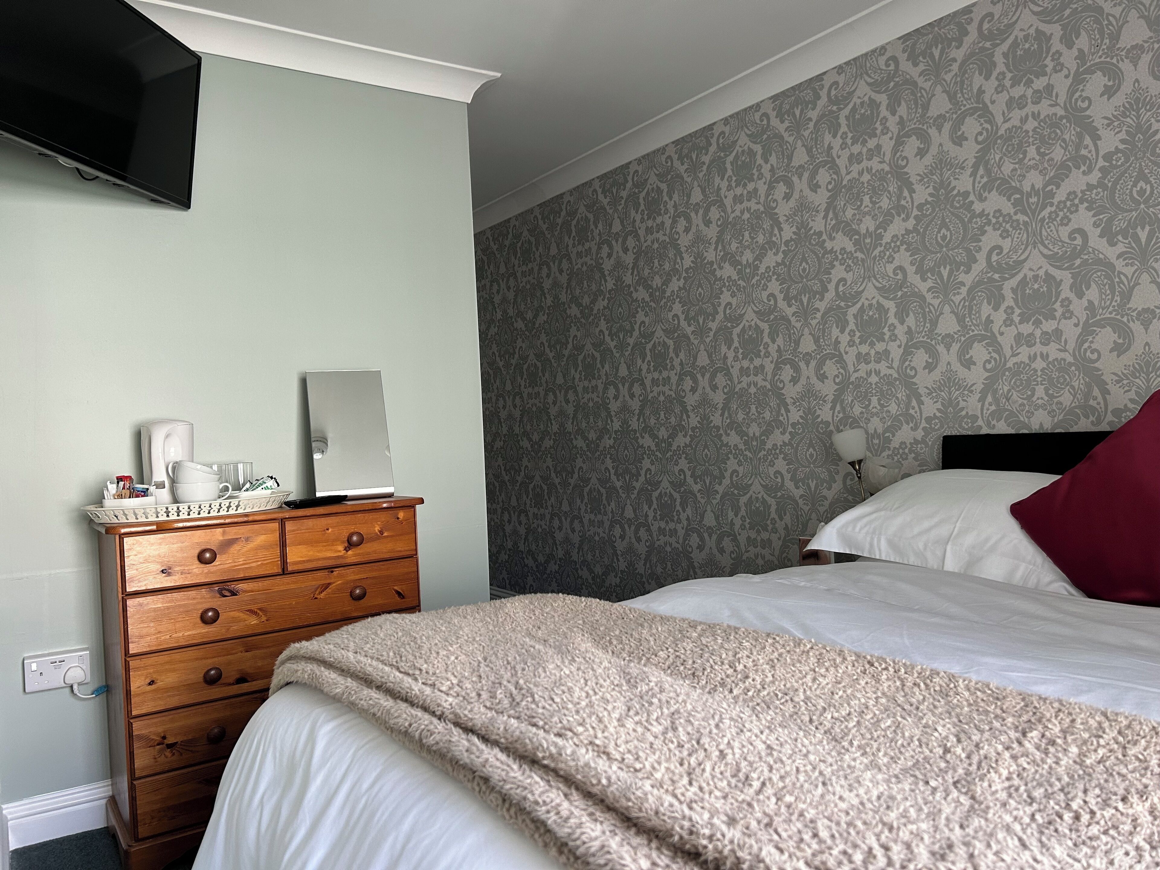 Quarto com cama, penteoudeiro, TV de tela plana na parede e papel de parede estampado.