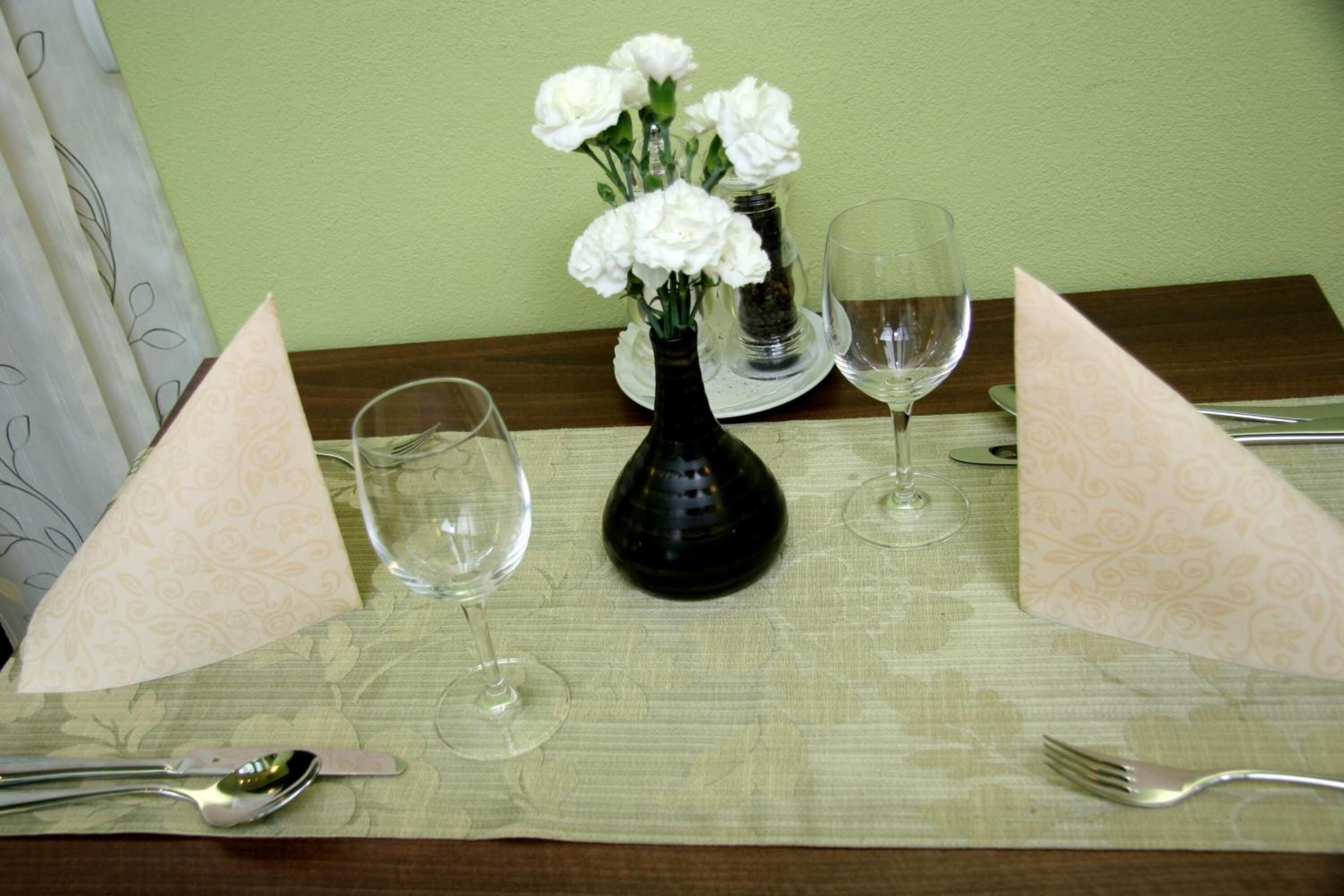 A table set with a vase of white flowers, two wine glasses, and cutlery.