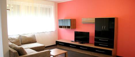 A living room with a sofa, TV, and entertainment unit against a pink wall.