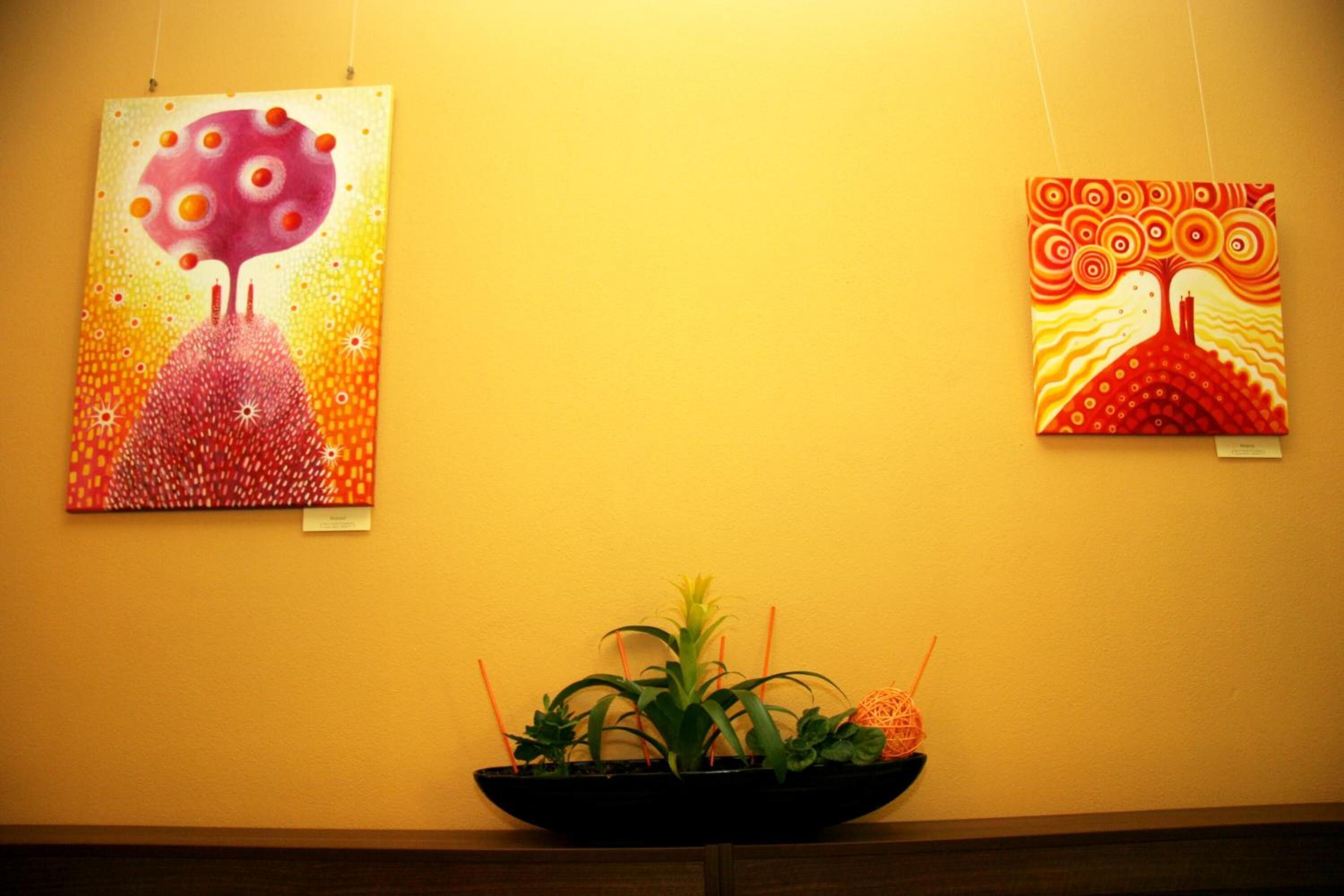 Twee kunstwerken aan een muur, een potplant op de voorgrond.