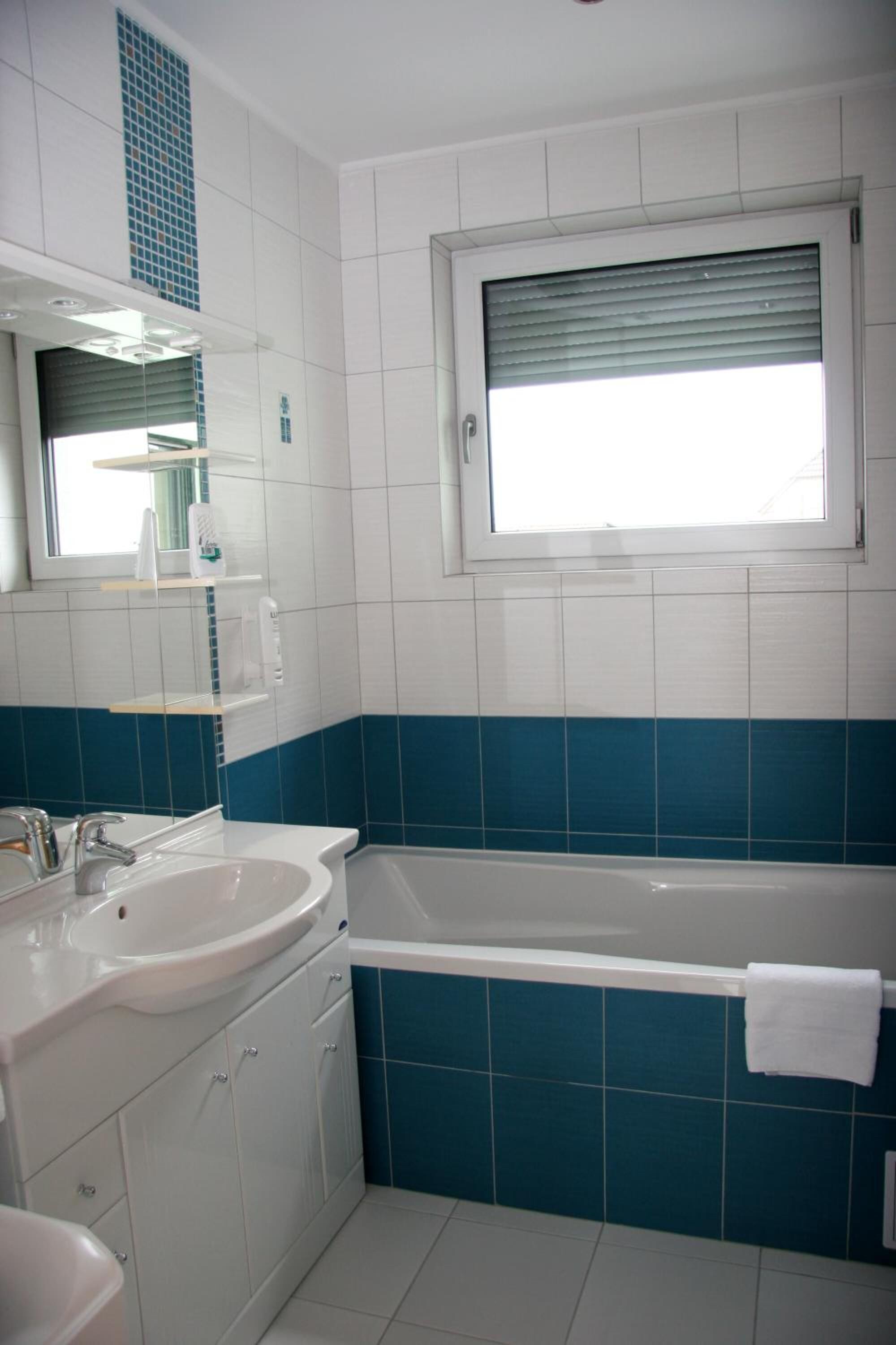 A bathroom with a white sink, a bathtub, and a window with blinds.