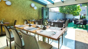 An outdoor dining area with wicker chairs and tables, a glass ceiling, and a view of the street. - Fine Restaurant & Apartments (Malacky)