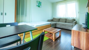 A modern, compact living space with a bed, sofa, dining table, and a TV. - Fine Restaurant & Apartments (Malacky)