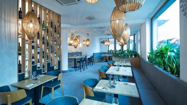 A restaurant with wooden shelves displaying bottles, hanging wicker chandeliers, and a view of greenery outside. - Fine Restaurant & Apartments (Malacky)