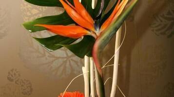 A floral arrangement with a bird of paradise flower, orange gerbera daisies, and green leaves in a vase.