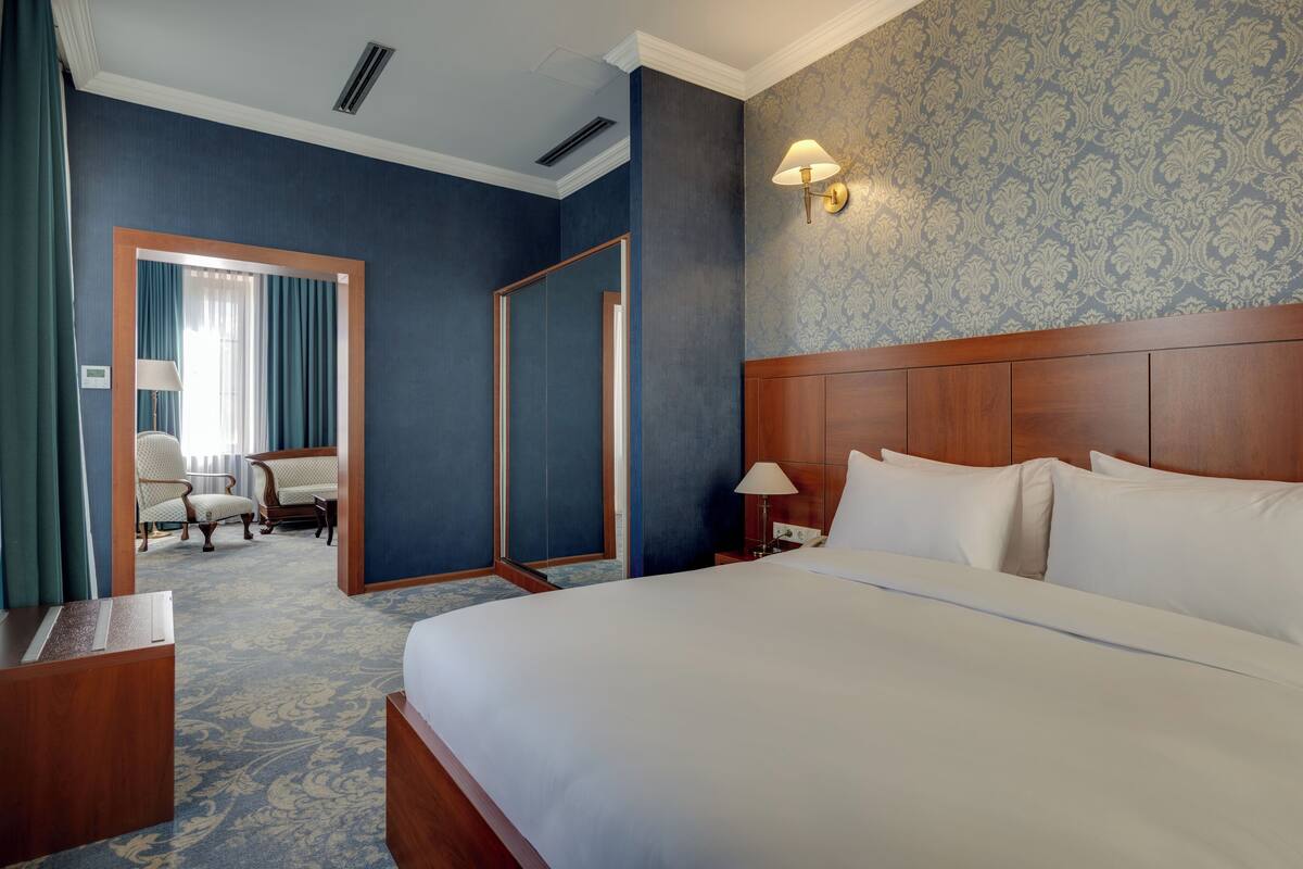 Une chambre d’hôtel avec un grand lit, un coin salon avec des fauteuils, un miroir et une lampe fixée au mur.