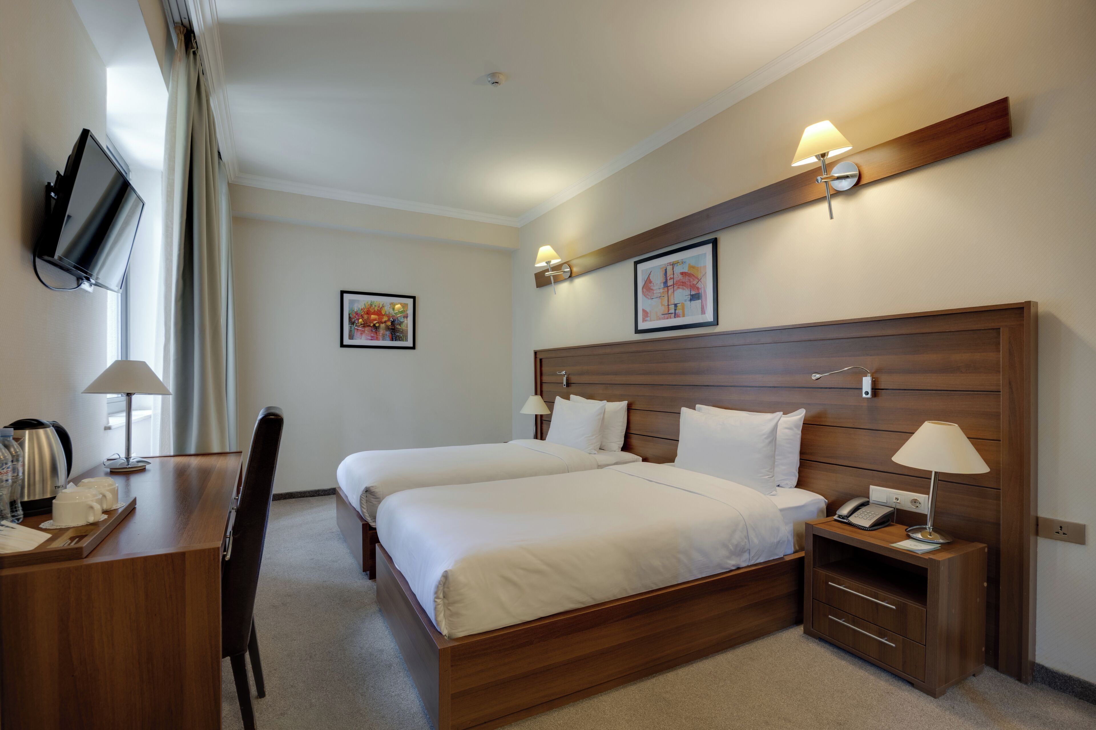 A hotel room with two beds, a desk with a telephone, a lamp, and a TV mounted on the wall.