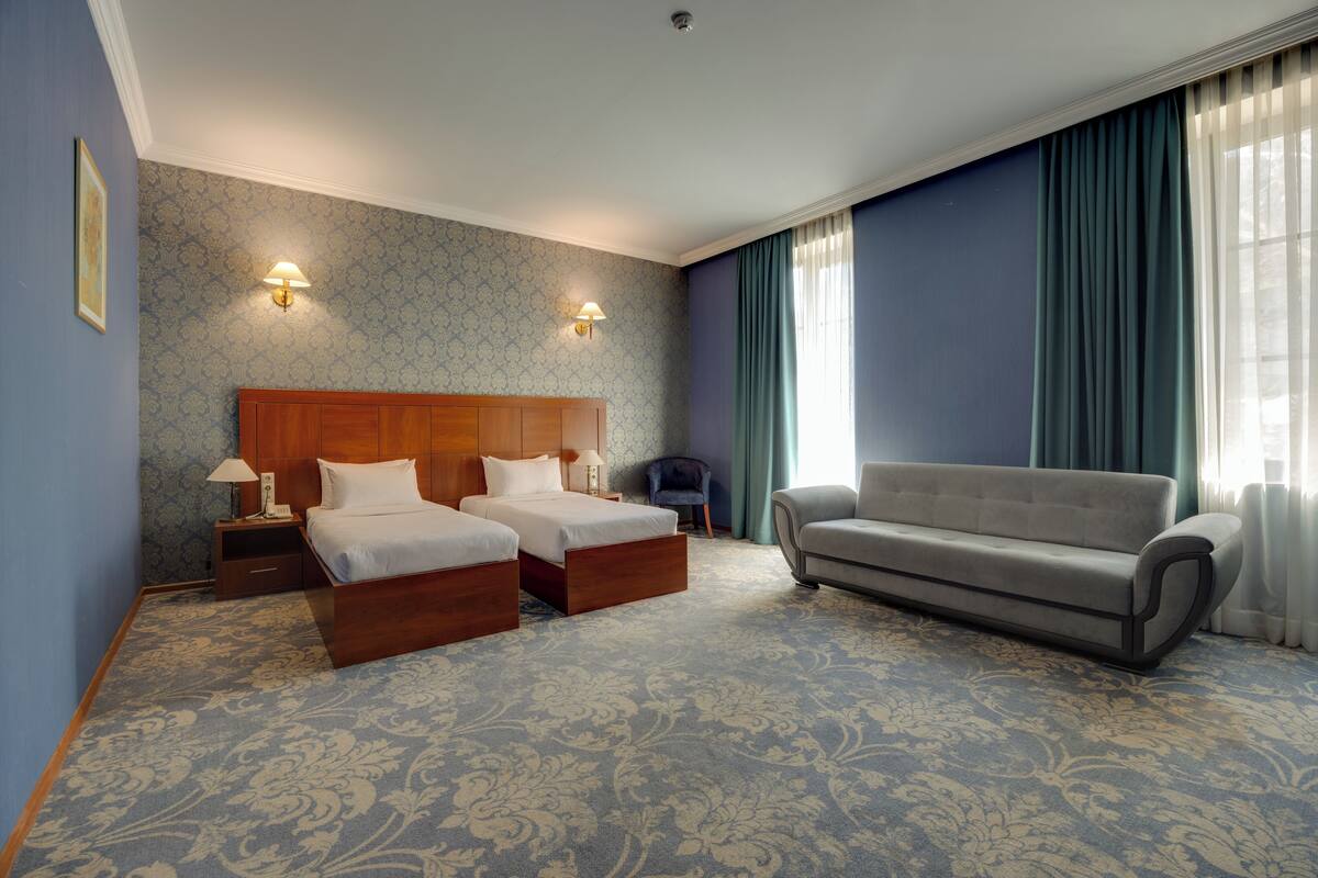 Une chambre d’hôtel avec deux lits, un canapé, une table de chevet avec une lampe et une moquette à motifs.