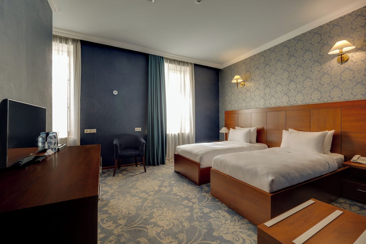 Une chambre d’hôtel avec deux lits, un bureau, une chaise, une télévision et une lampe.