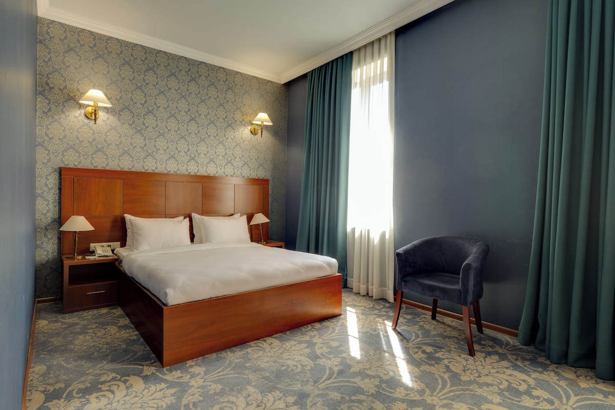 Une chambre d’hôtel avec un grand lit, deux tables de chevet avec des lampes, une chaise et une fenêtre avec des rideaux.