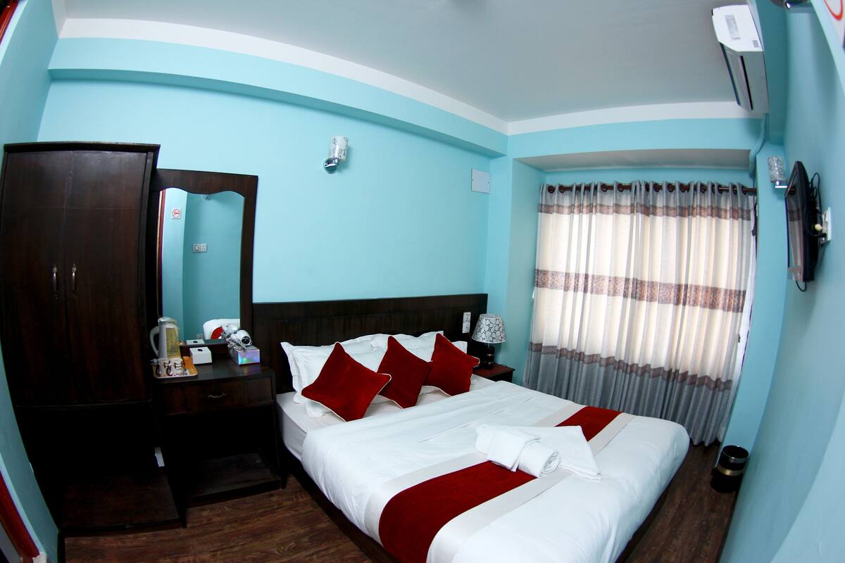 A hotel room with a large bed, a wardrobe, a bedside table with a lamp, and a window with curtains.