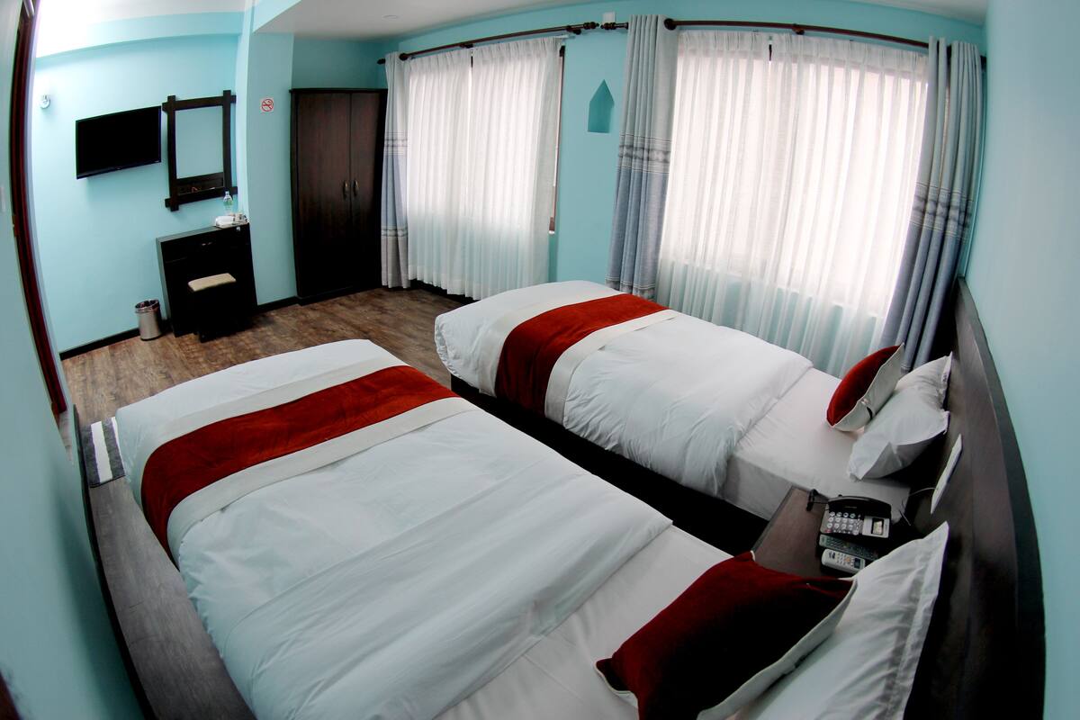 A hotel room with two beds, a TV, a desk with a phone, and a window with curtains.