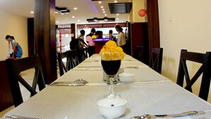 A restaurant with a long table set for dining, featuring a centerpiece with yellow flowers and a glass of red wine.