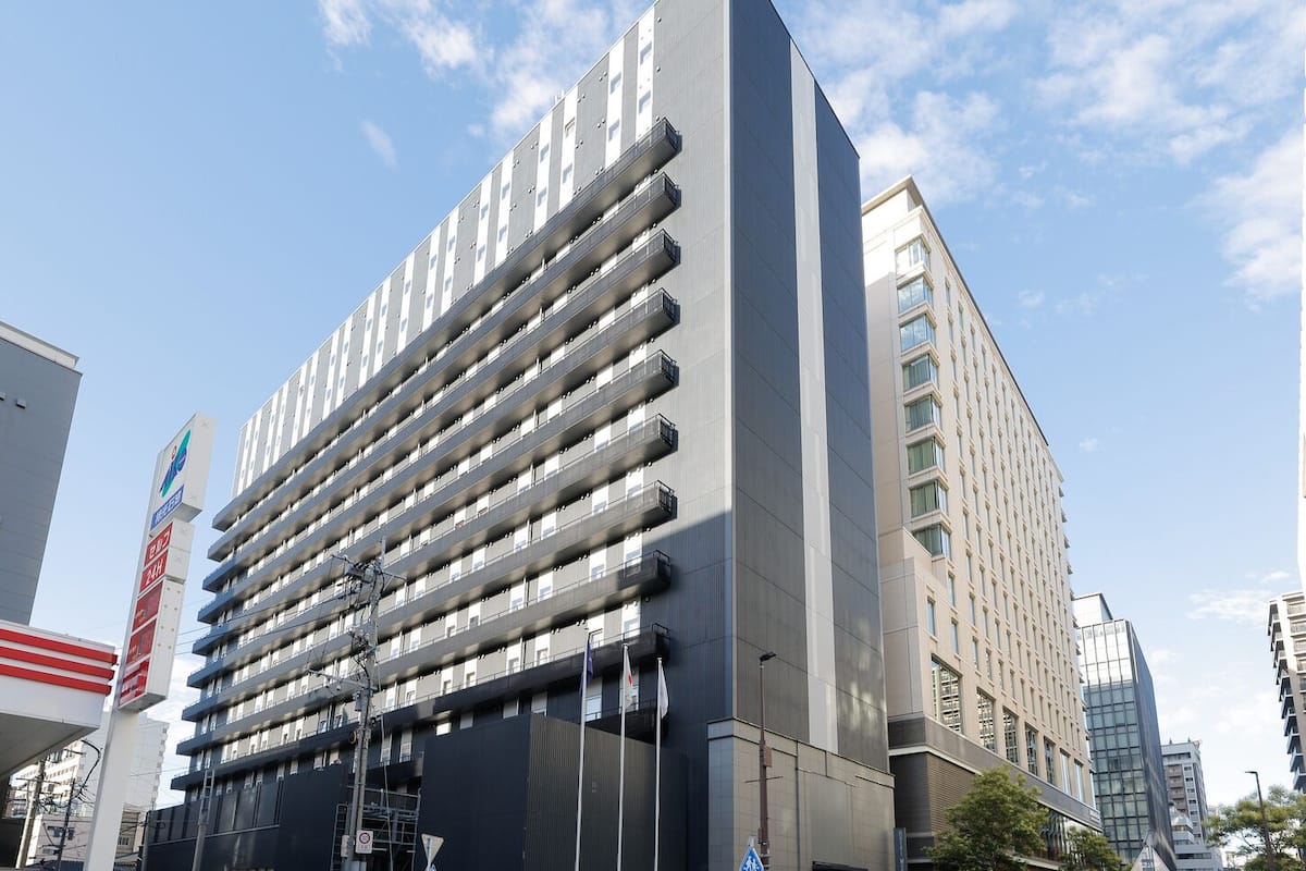 Un immeuble à plusieurs étages doté d’une architecture moderne, caractérisé par une série de balcons et un élément vertical marquant sur le côté gauche.