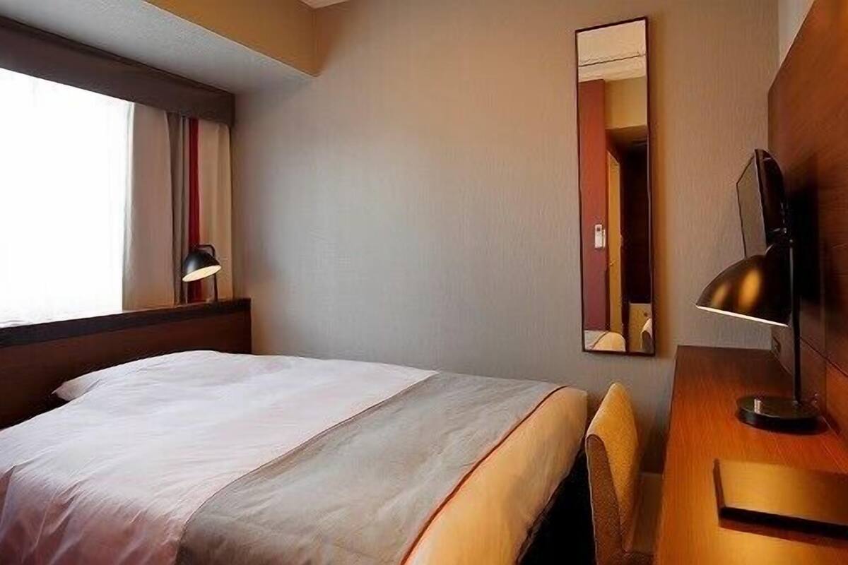 Une chambre d’hôtel équipée d’un lit, d’un bureau, d’une chaise, d’une télévision et d’un miroir.