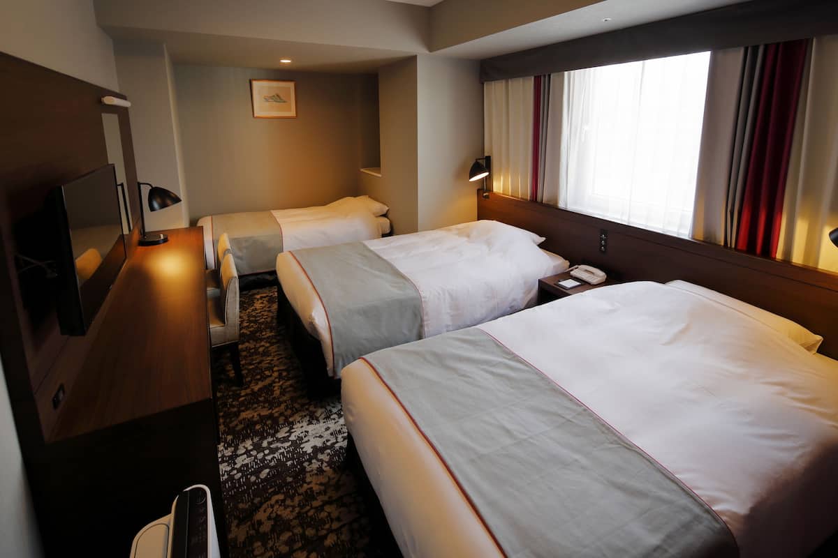 Une chambre d’hôtel avec deux lits, un bureau avec une lampe, un téléphone et une fenêtre avec des rideaux.