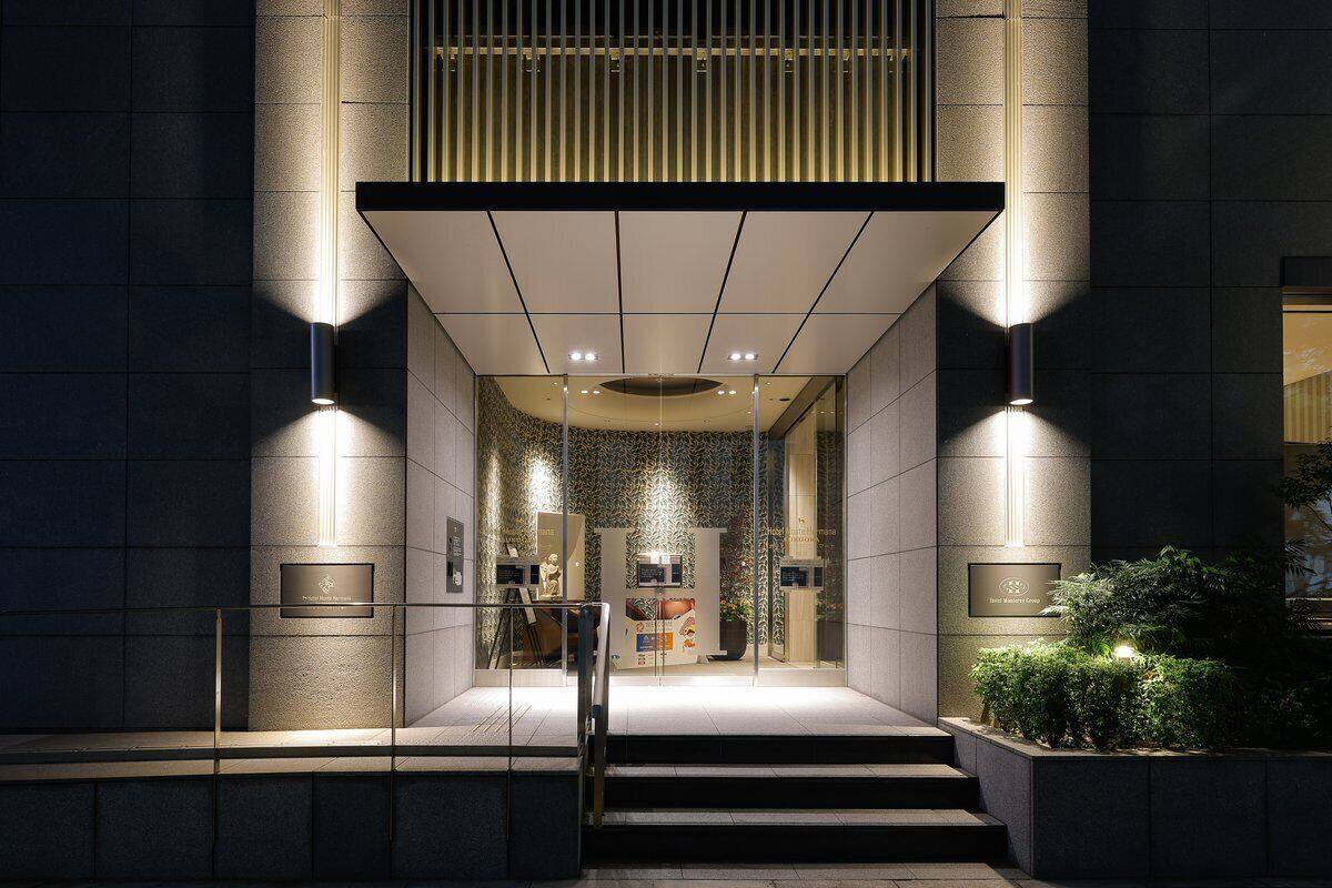 L’entrée d’un hôtel au design moderne, caractérisée par une façade en verre, un escalier menant à l’entrée et un intérieur bien éclairé, visible à travers le verre.