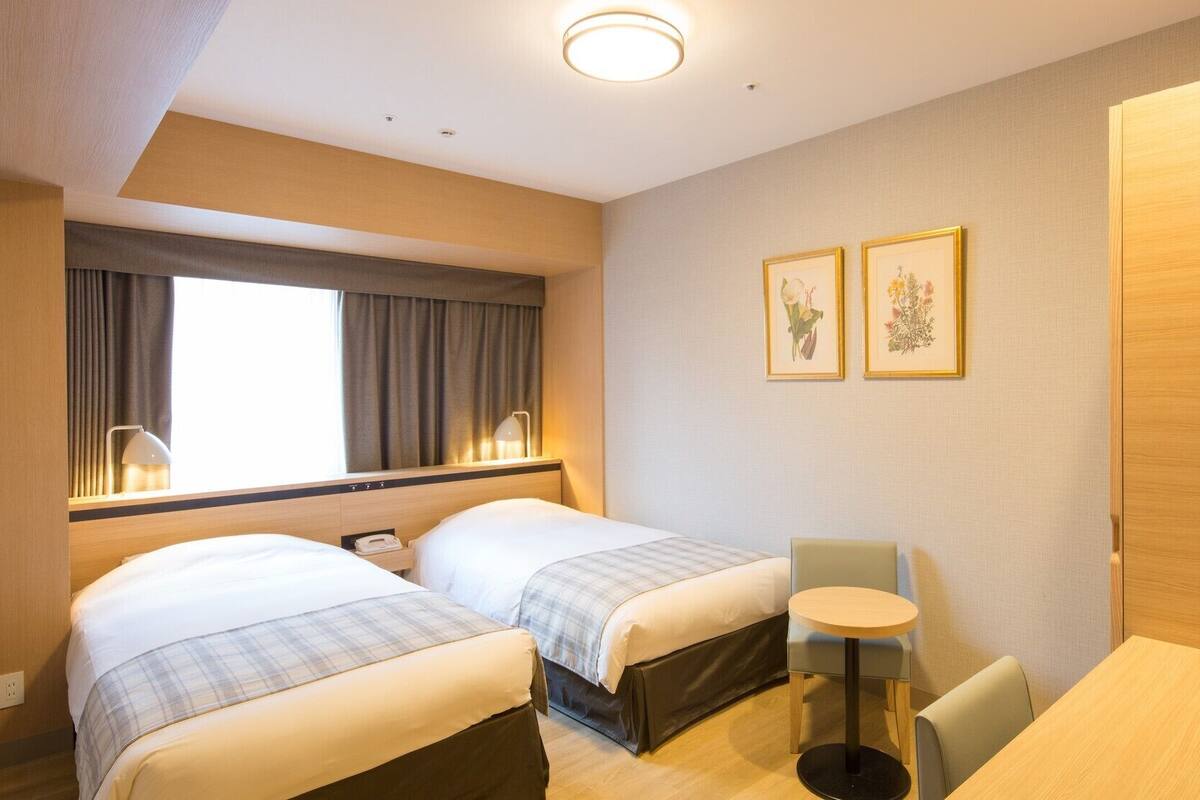 Une chambre d’hôtel avec deux lits, une petite table, une chaise, un téléviseur et une fenêtre avec des rideaux.