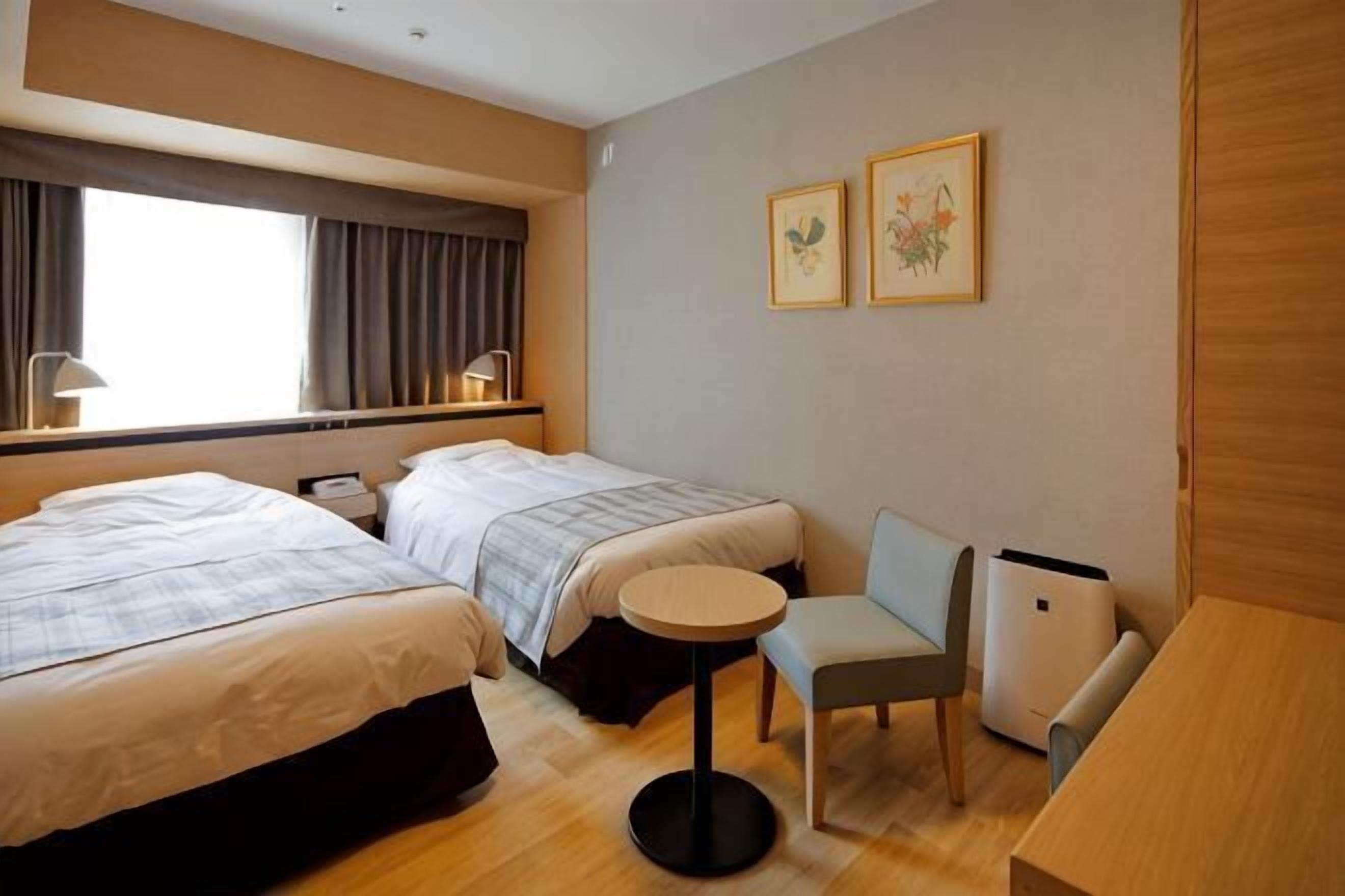 Ein Hotelzimmer mit zwei Betten, einem kleinen runden Tisch, einem Stuhl und einem Schreibtisch.