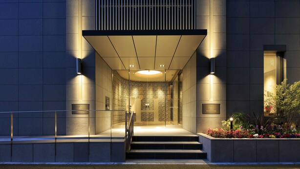 A modern building entrance with a glass facade, a set of stairs leading to the entrance, and a landscaped area with plants. - Hotel Monte Hermana Fukuoka (Fukuoka)