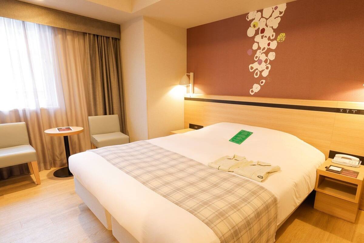 Une chambre d’hôtel avec un grand lit, une table de chevet avec une lampe, une chaise et une petite table.