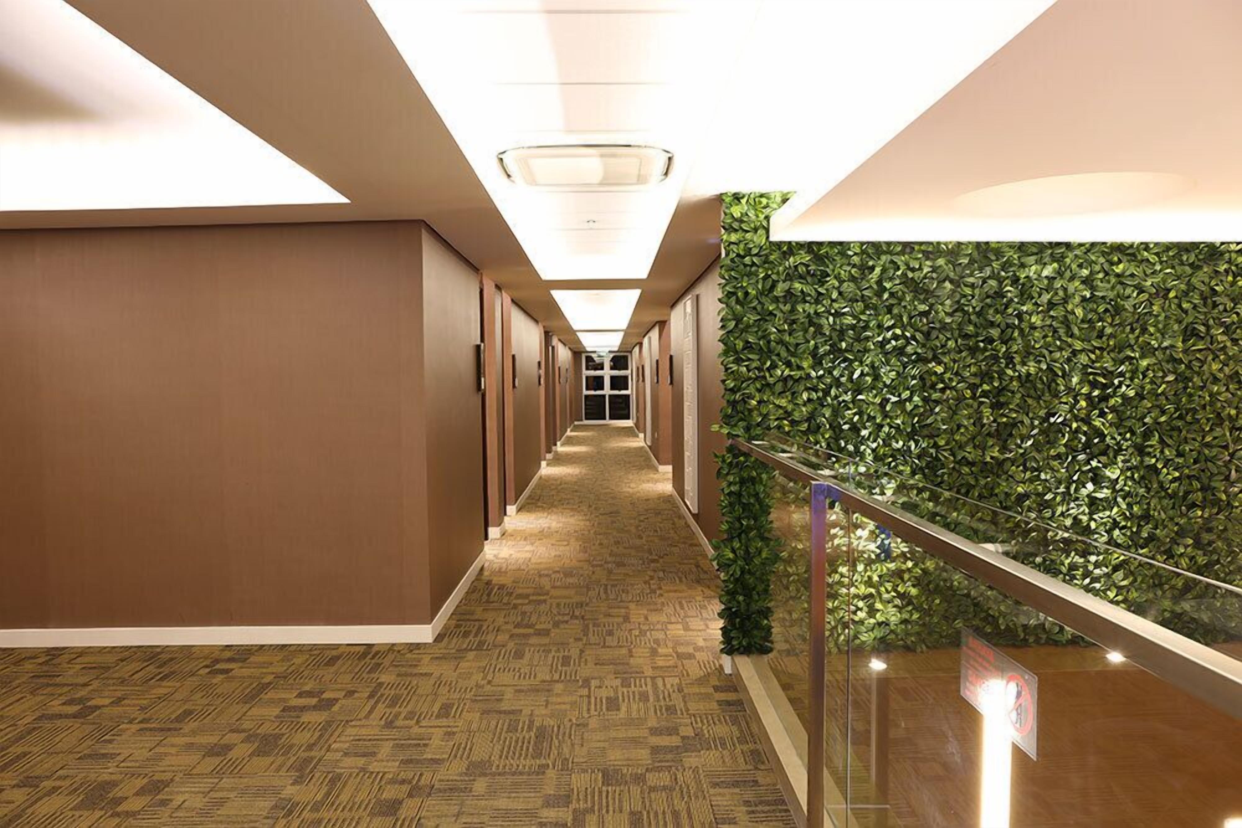 A hallway with a patterned carpet, wooden walls, and a green wall with foliage.