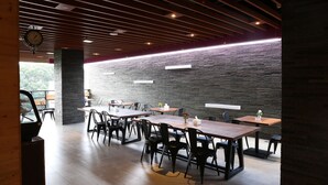 Un restaurante moderno con mesas y sillas de madera, una pared de ladrillo y un reloj en el techo.