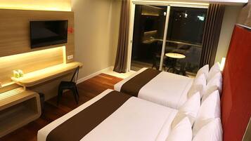 Habitación de hotel con dos camas, un televisor montado en la pared, un escritorio con una silla y una pequeña mesa con sillas.