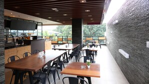 Un espacio de comedor al aire libre con mesas y sillas de madera, un muro de ladrillo y una cocina moderna con televisor de pantalla plana.