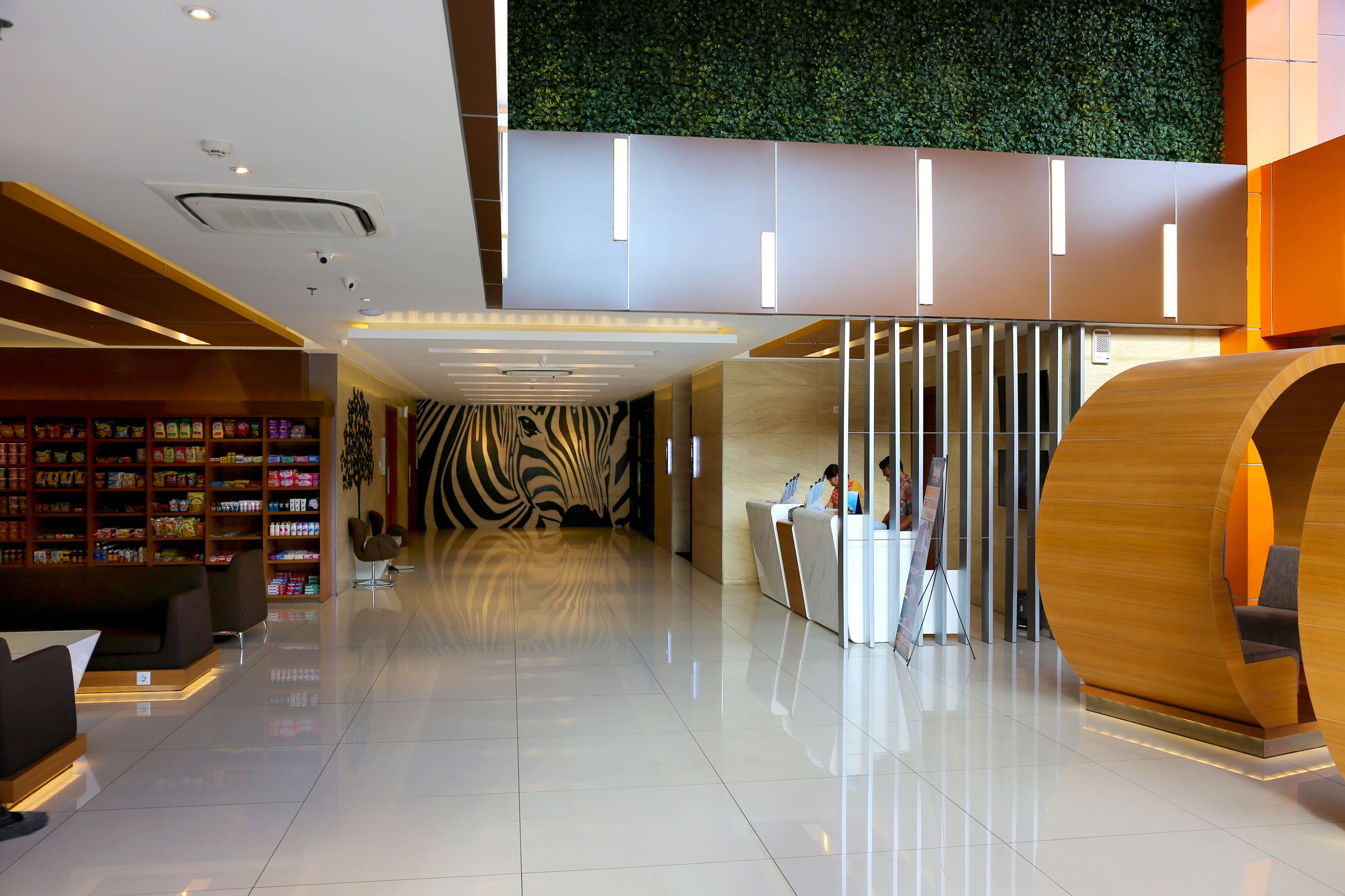 Een moderne lobby met een receptiebalie, zithoek en een muur met een weelderig, groen ontwerp.
