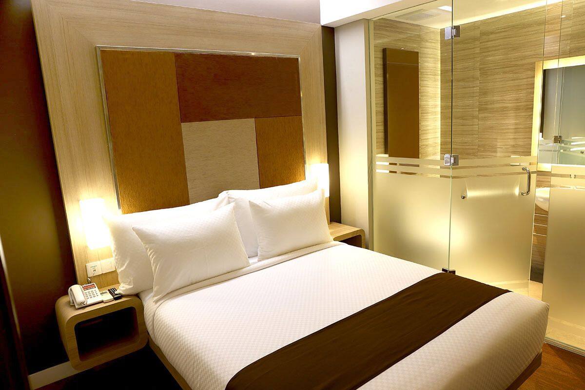 A hotel room with a large bed, a bedside table with a phone, and a glass-enclosed walk-in closet.