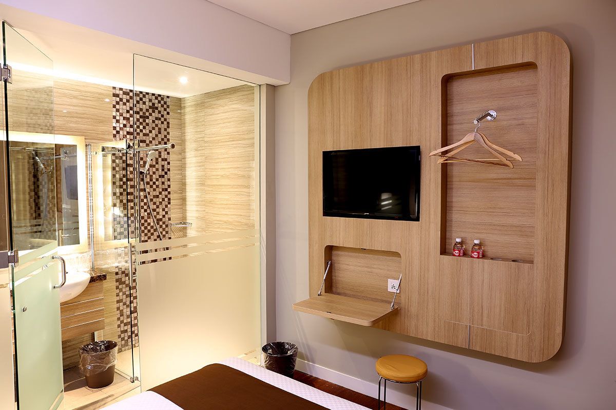 Un bagno moderno con box doccia in vetro, una TV a parete e scaffali contenitori in legno.