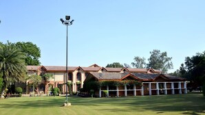 A large building with multiple sections, including a covered area with columns and a lawn in front. - Ashok Country Resort (New Delhi)