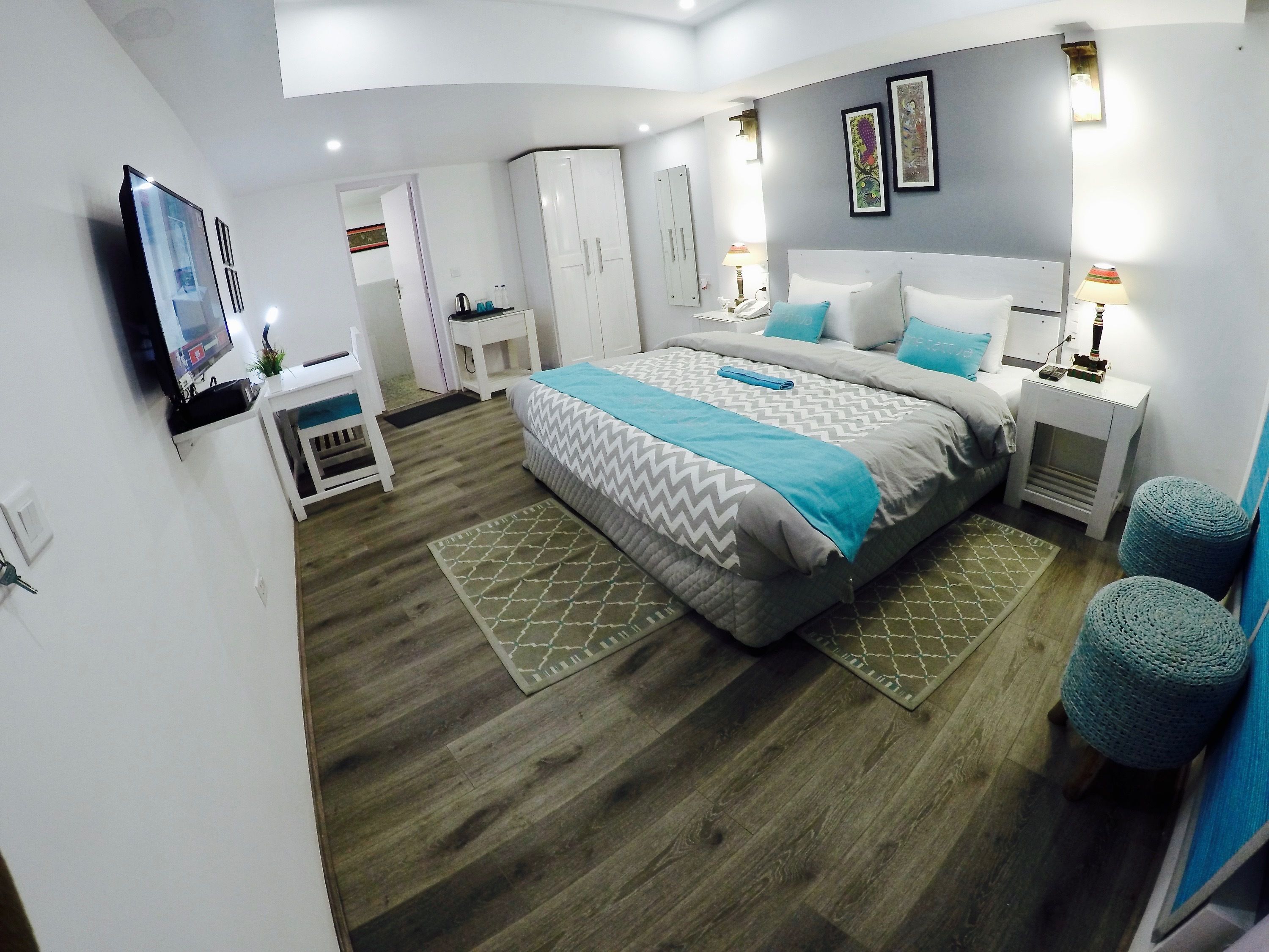 A modern bedroom with a large bed, a TV mounted on the wall, a wardrobe, and a desk with a chair.