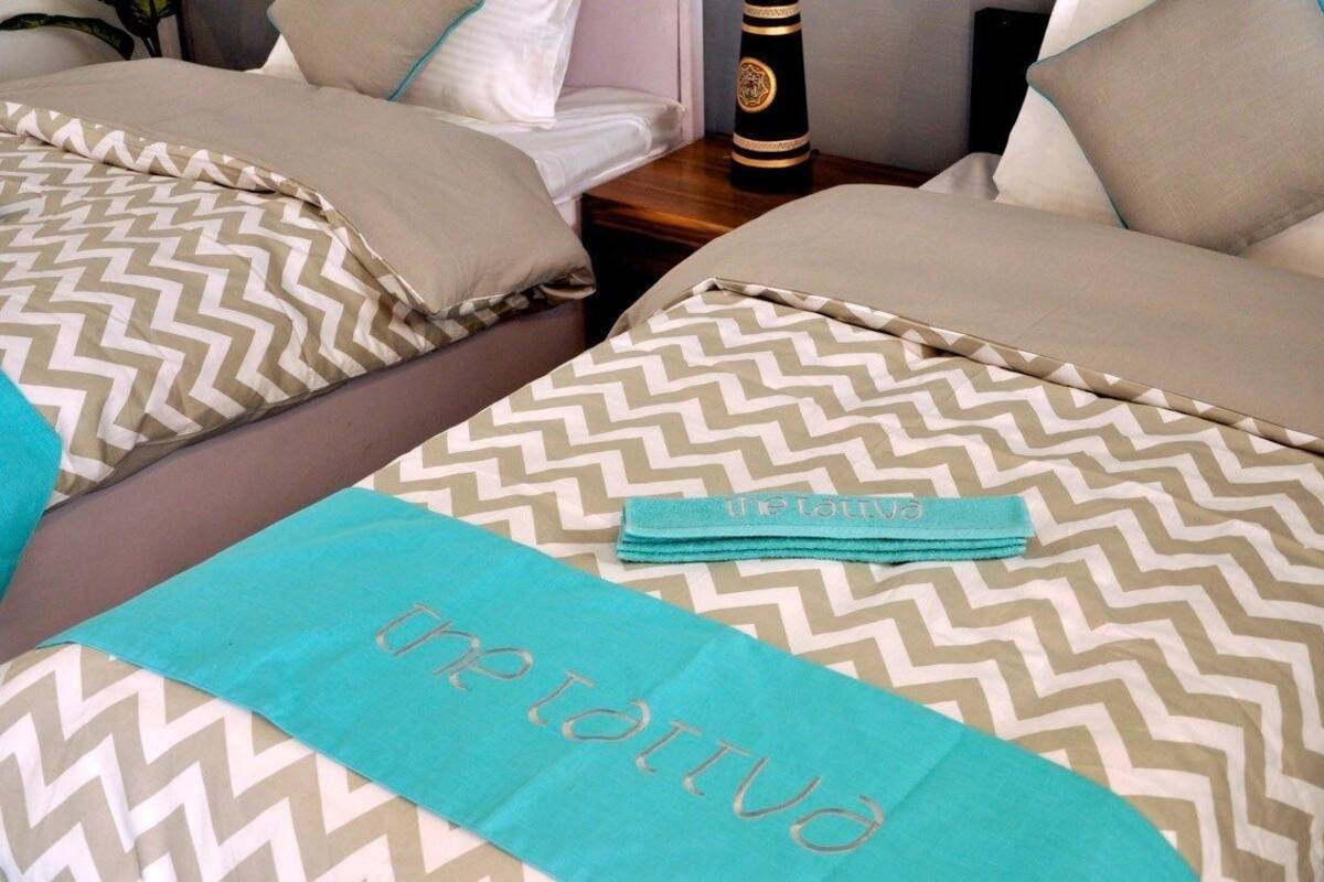 Habitación de hotel con dos camas, cada una con ropa de cama estampada y una toalla color turquesa.