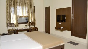Quarto de hotel com cama, escrivaninha com cadeira, televisão fixada na parede e um guarda-roupa espaçoso.