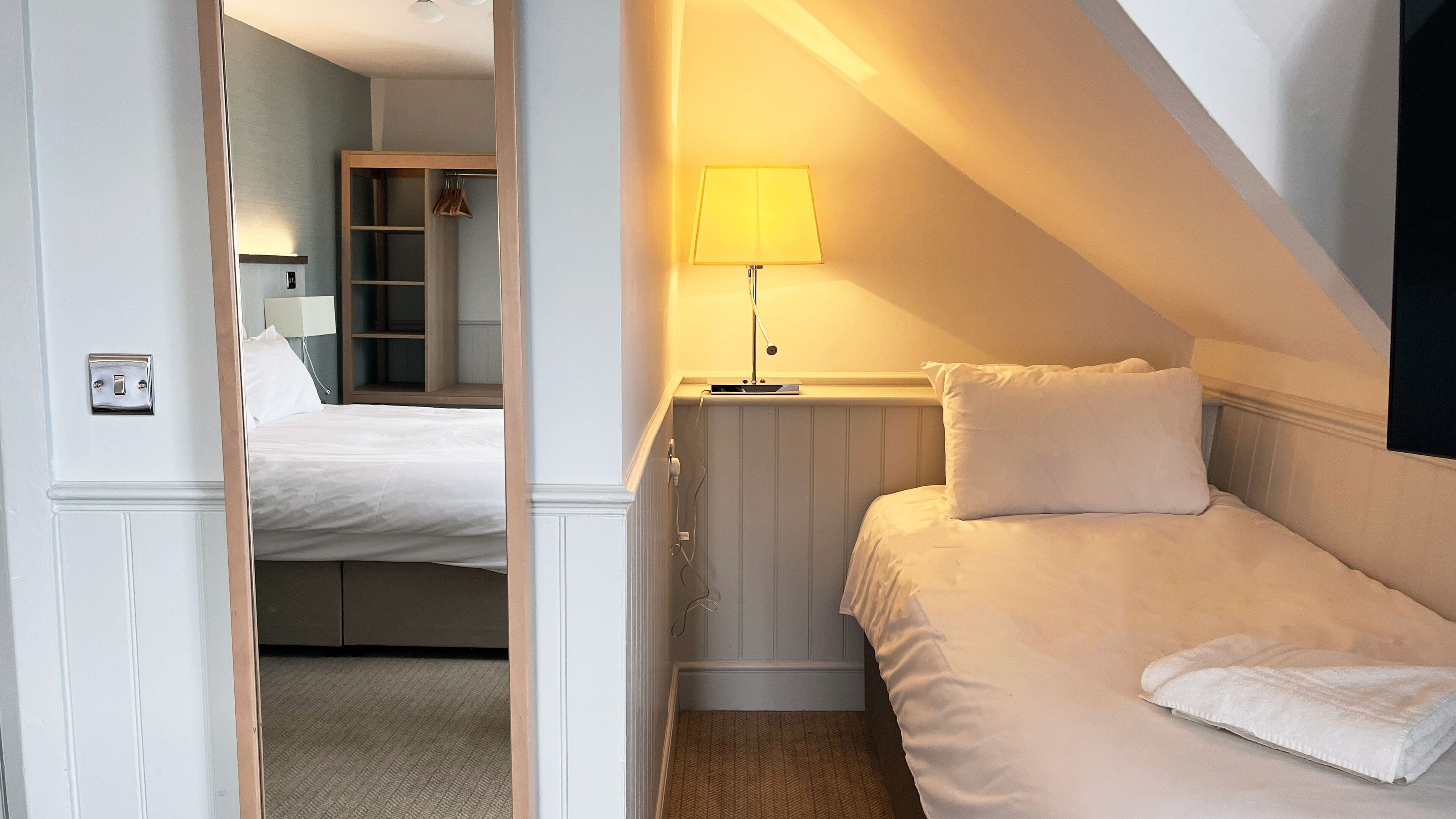 A bedroom with a bed, a bedside table with a lamp, a wardrobe, and a mirror.