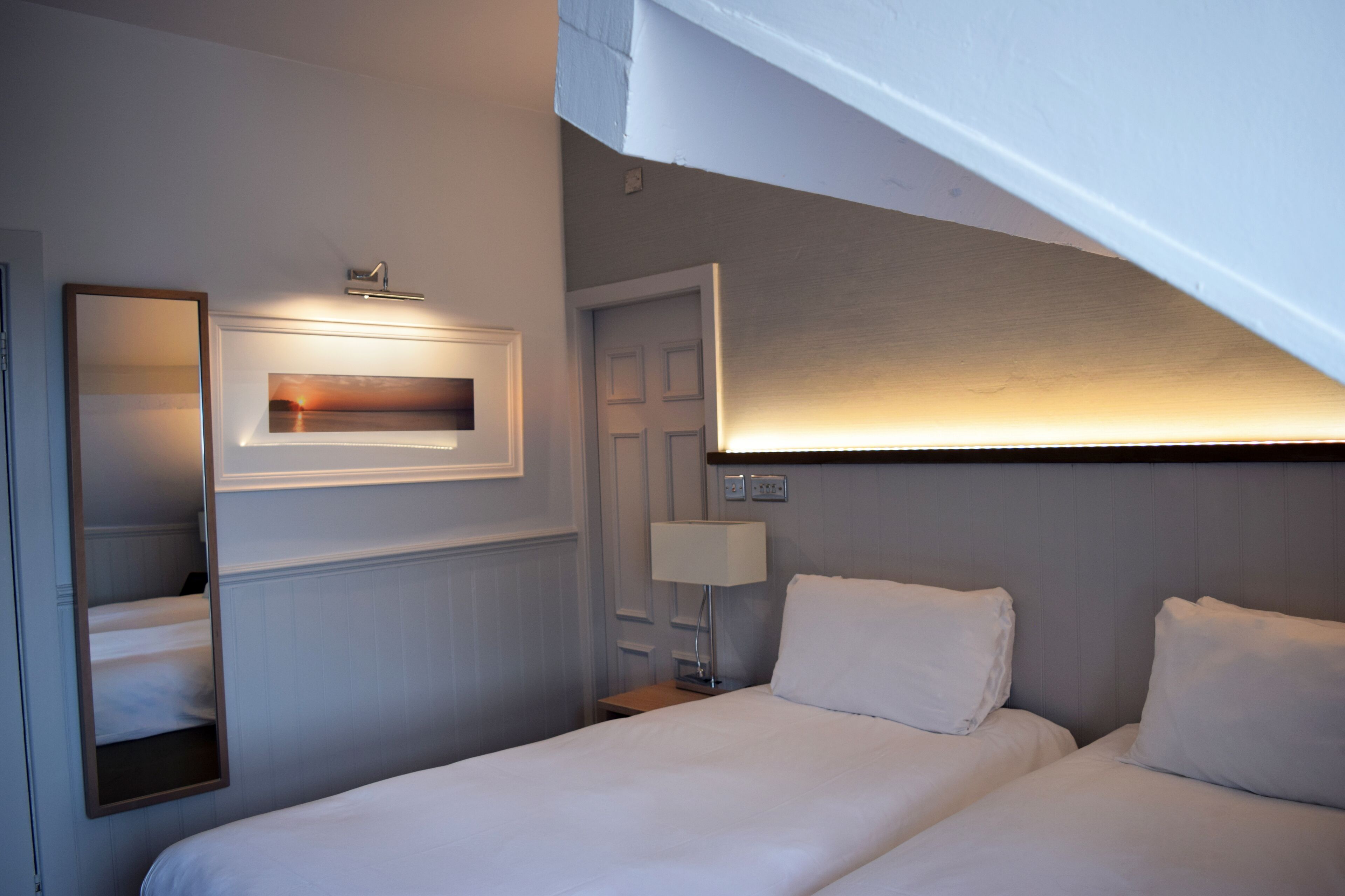 Una habitación de hotel con cama, mesita de noche, lámpara, espejo y puerta.