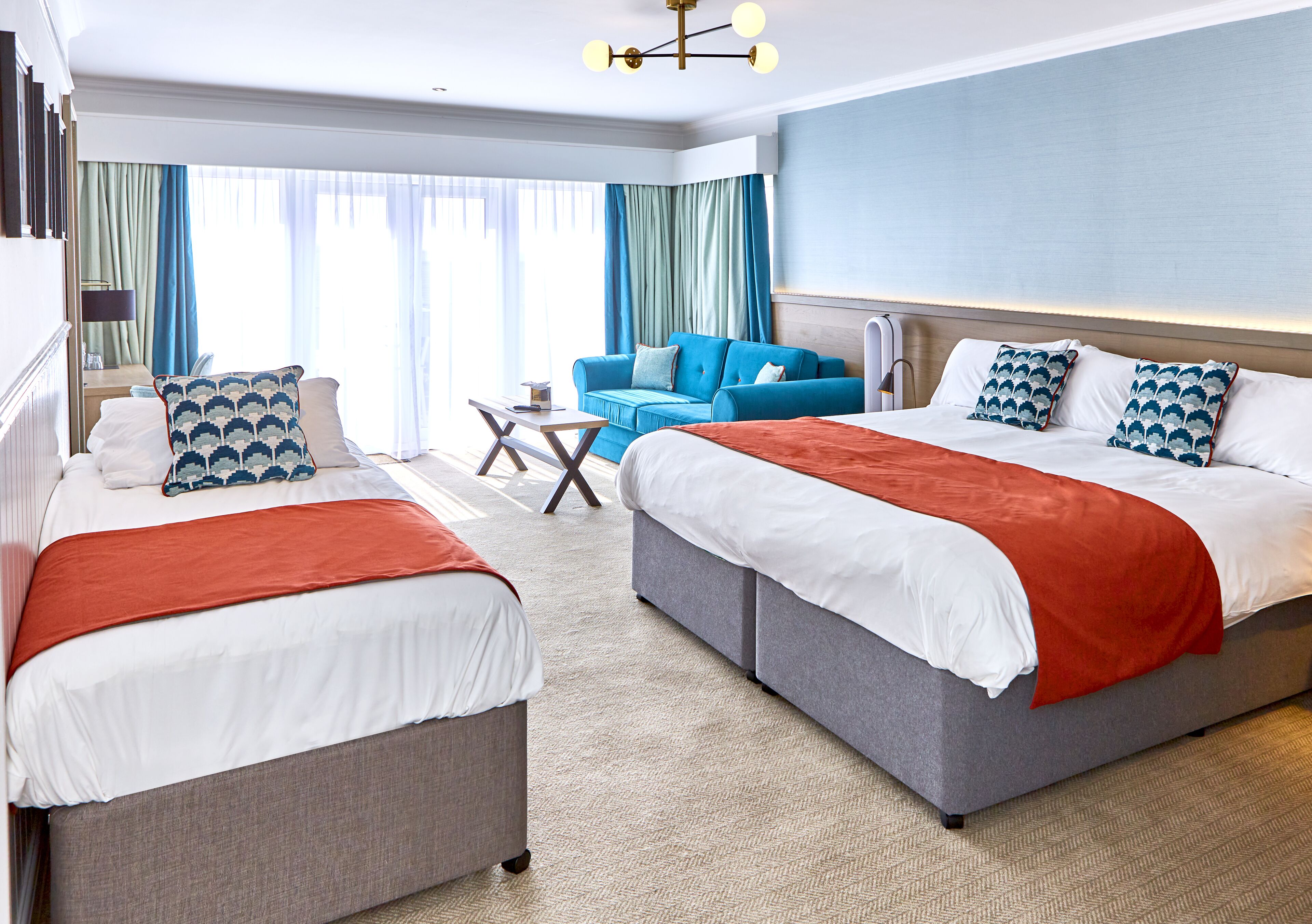 Ein Hotelzimmer mit zwei Betten, einem Sofa, einem kleinen Tisch und Blick ins Freie.