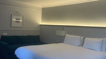 Una habitación de hotel con una cama grande, un sofá verde, un aplique de techo y una lámpara de pared.