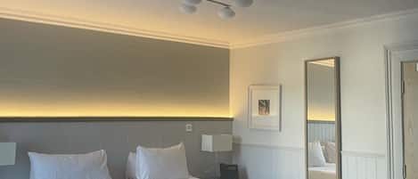 A hotel room with a large bed, bedside tables, a ceiling light fixture, a wall-mounted mirror, and a door.