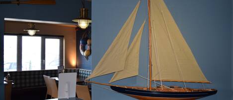 Un velero modelo sobre una encimera en una habitación con paredes azules y un ventanal.