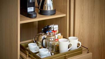 A wooden cabinet with a tray containing a coffee maker, a glass carafe, cups, and a box of coffee pods.