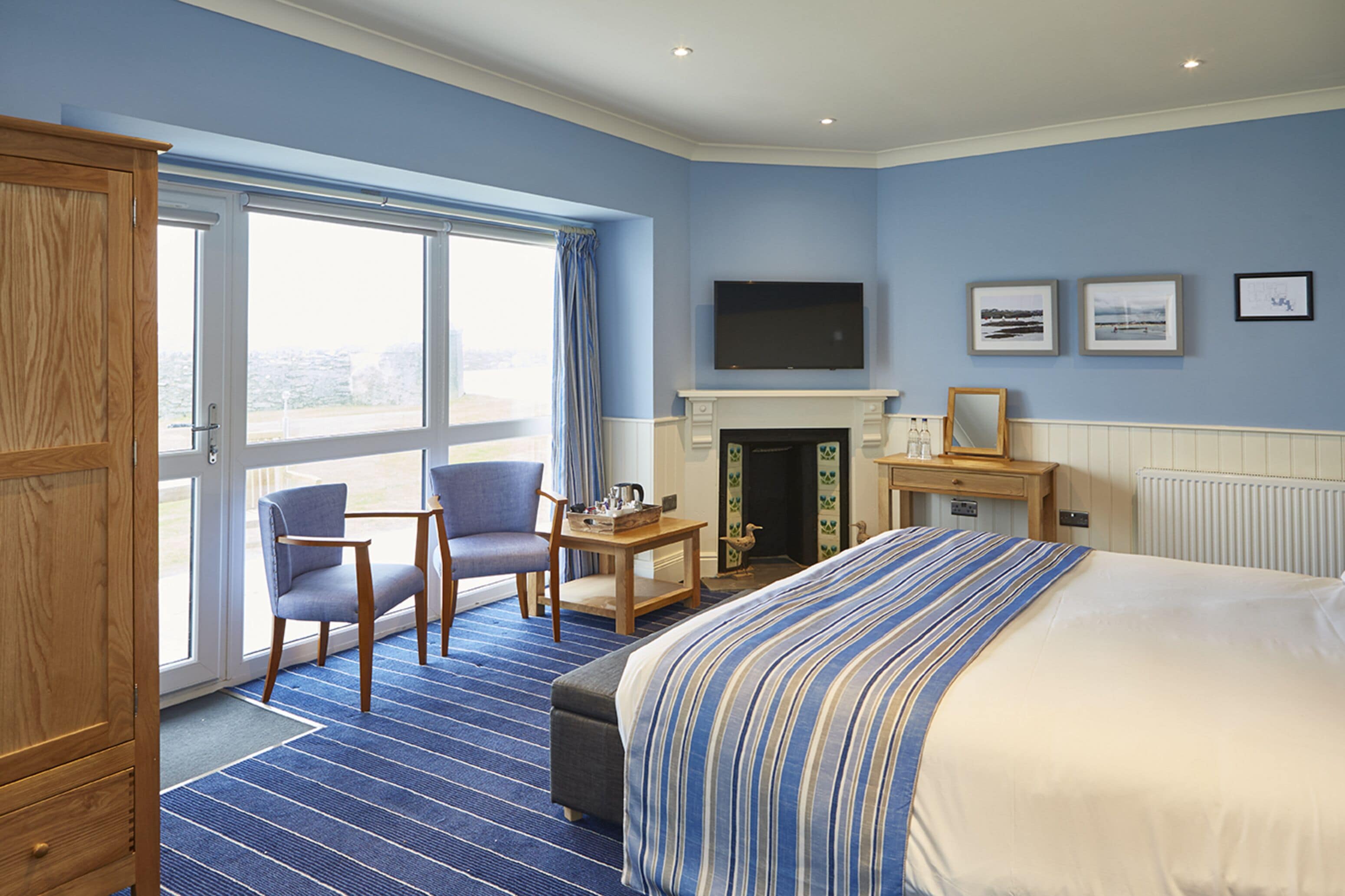 A hotel room with a large bed, two chairs, a fireplace, a television, and a view through the window.