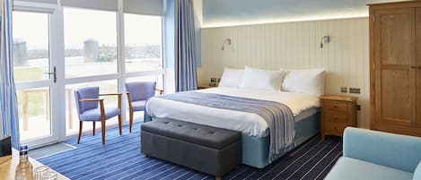 Habitación de hotel con una cama grande, un sofá, una mesita con vasos y una botella, y vistas a través de puertas de cristal.