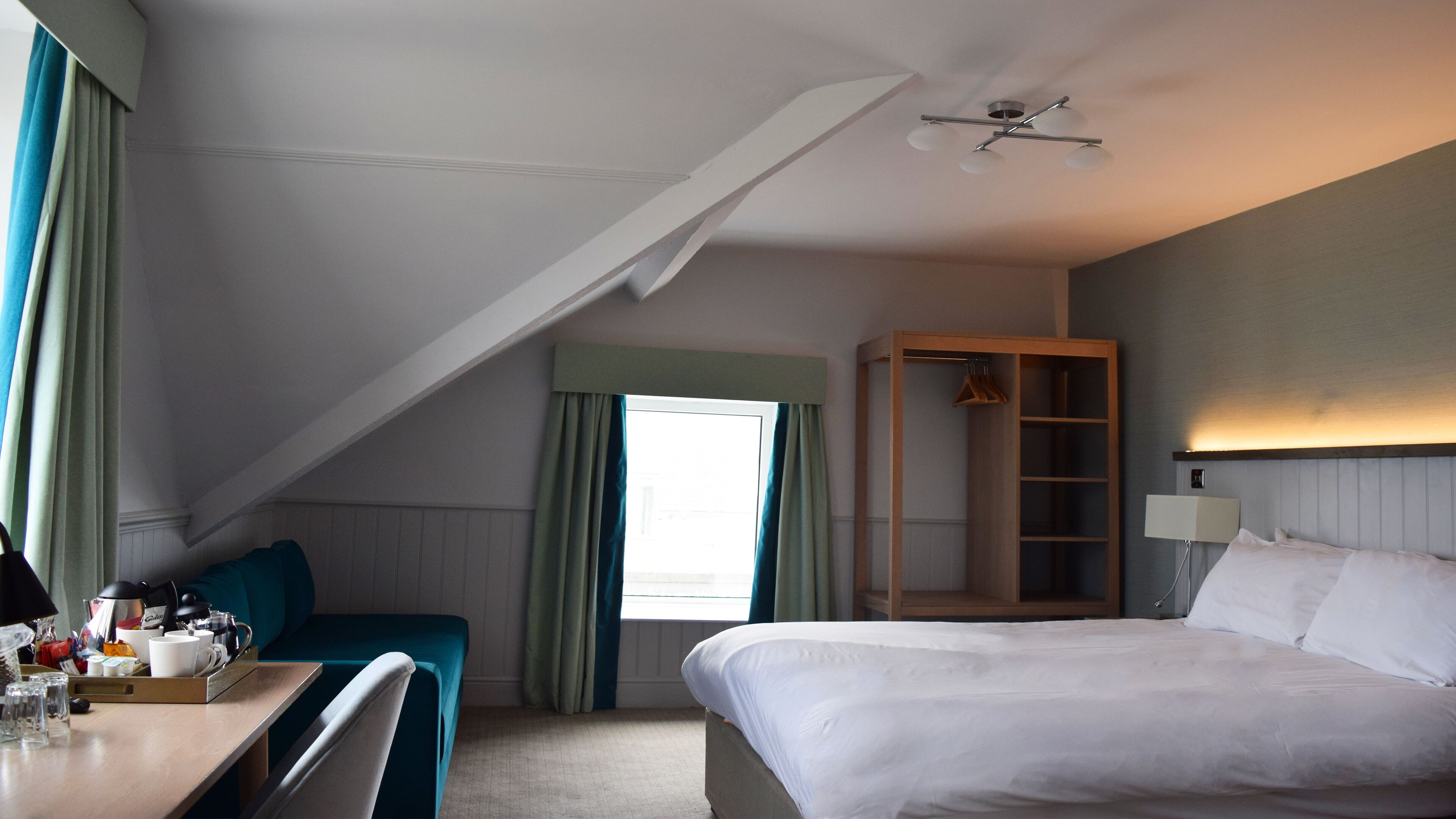 Une chambre d’hôtel comprenant un lit, un bureau avec une chaise, une armoire et un ventilateur de plafond.